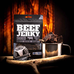 Kuivalihakundi Beef Jerky Røkt foran flammer, med stålkopp fylt med jerkybiter
