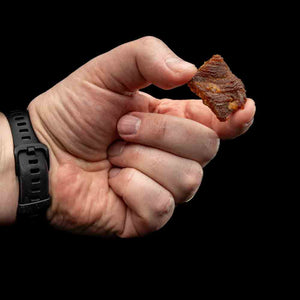Hånd holder en bit Kuivalihakundi Greasy Pork Jerky Koreansk Stil mot sort bakgrunn