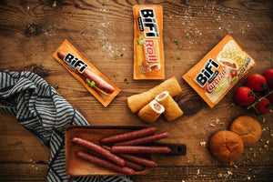 BiFi Original pølsesnacks på et trebord, sett ovenfra med brød og tomater