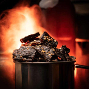 Stålkopp fylt med Kuivalihakundi teriyaki beef jerky foran flammer