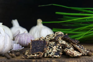 Nærbilde av Kuivalihakundi beef jerky med hvitløk ved hvitløksløker og gressløk på mørk bakgrunn