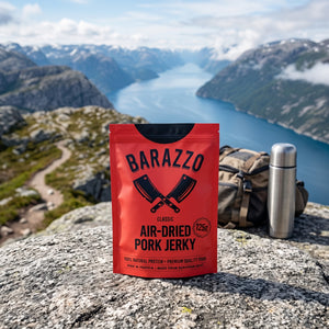 Barazzo Tørket Svinefilet Klassisk på en stein ved en fjellsti høyt over fjorden, med ryggsekk og termos, AI-generert bilde