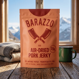 Barazzo Tørket Svinefilet BBQ på et trebord i en hytte, med ullpledd, emaljekopp og snødekte fjell utenfor vinduet, AI-generert bilde