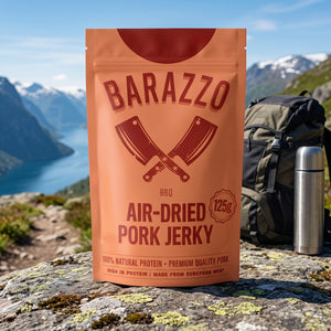 Barazzo Tørket Svinefilet BBQ på en stein ved en fjellsti høyt over fjorden, med ryggsekk og termos, AI-generert bilde