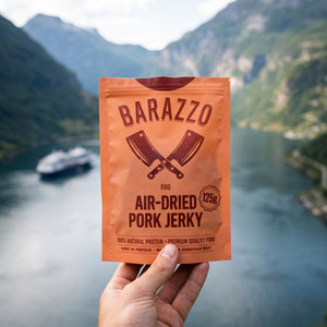 Hånd som holder Barazzo Tørket Svinefilet BBQ foran et fjordlandskap, AI-generert bilde