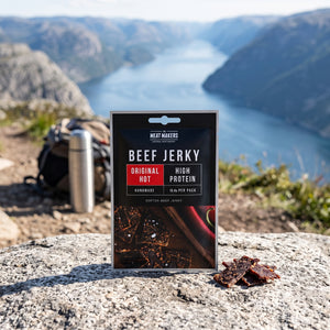 Meat Makers Beef Jerky Hot på en stein ved en fjellsti høyt over fjorden, med ryggsekk og termos, AI-generert bilde