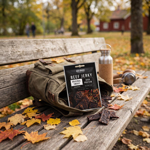 Meat Makers Beef Jerky Smoky stikker opp av en ryggsekk på en parkbenk om høsten, med drikkeflaske og hodetelefoner, AI-generert bilde