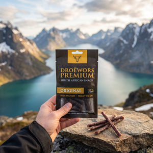 Hånd som holder Biltong Premium Original Ølpølse (Droëwors) foran et fjordlandskap, AI-generert bilde