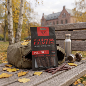 Biltong Premium Piri Piri Ølpølse (Droëwors) stikker opp av en ryggsekk på en parkbenk om høsten, med drikkeflaske og hodetelefoner, AI-generert bilde