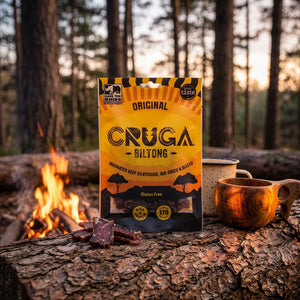 Cruga Biltong Original på en stokk ved bålet i furuskogen i skumringen, med emaljekopp og kuksa, AI-generert bilde