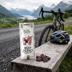 Fine Gusto Beef Jerky Naturell på en benk ved grusveien, med sykkel og sykkelhjelm, AI-generert bilde