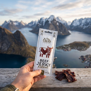 Hånd som holder Fine Gusto Beef Jerky Naturell foran et fjordlandskap, AI-generert bilde