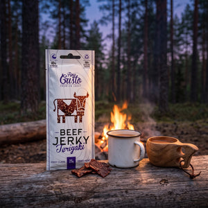 Fine Gusto Beef Jerky Teriyaki på en stokk ved bålet i furuskogen i skumringen, med emaljekopp og kuksa, AI-generert bilde