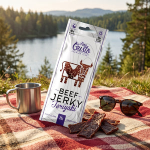 Fine Gusto Beef Jerky Teriyaki på et rutete piknikteppe ved et skogsvann en sommerdag, med stålkopp og solbriller, AI-generert bilde