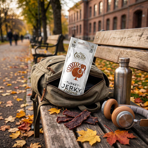 Fine Gusto Kalkun Jerky Naturell stikker opp av en ryggsekk på en parkbenk om høsten, med drikkeflaske og hodetelefoner, AI-generert bilde
