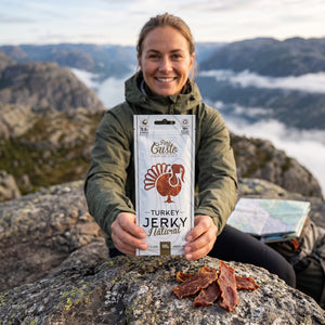 Turgåer tar en pause på fjellet og holder Fine Gusto Kalkun Jerky Naturell, AI-generert bilde
