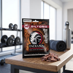 Indiana Biltong Original på en benk på treningssenteret, med manualer, håndkle og drikkeflaske i bakgrunnen, AI-generert bilde
