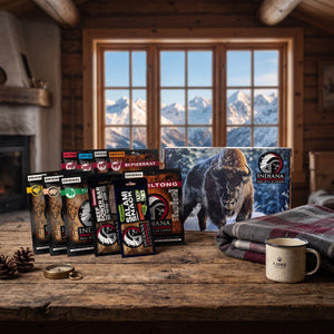 Indiana Jerky Gavepakning på et trebord i en hytte, med ullpledd, emaljekopp og snødekte fjell utenfor vinduet, AI-generert bilde