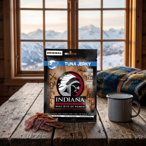 Indiana Tunfisk Jerky Original på et trebord i en hytte, med ullpledd, emaljekopp og snødekte fjell utenfor vinduet, AI-generert bilde