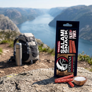 Indiana Salami Original på en stein ved en fjellsti høyt over fjorden, med ryggsekk og termos, AI-generert bilde