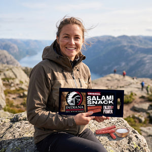 Turgåer tar en pause på fjellet og holder Indiana Salami Original, AI-generert bilde