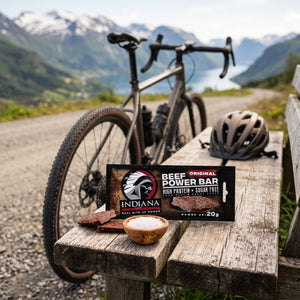 Indiana Beef Bar Original på en benk ved grusveien, med sykkel og sykkelhjelm, AI-generert bilde