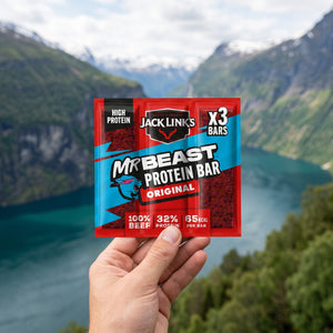 Hånd som holder Jack Link's Protein Bar 3-pack foran et fjordlandskap, AI-generert bilde