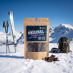 KJØ Teriyaki & Garlic Beef Jerky i snøen ved siden av turski og staver på en solrik vinterdag i fjellet, AI-generert bilde