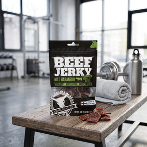 Kuivalihakundi Beef Jerky Mild Habanero på en benk på treningssenteret, med manualer, håndkle og drikkeflaske i bakgrunnen, AI-generert bilde