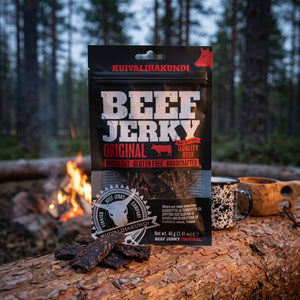 Kuivalihakundi Beef Jerky Original på en stokk ved bålet i furuskogen i skumringen, med emaljekopp og kuksa, AI-generert bilde