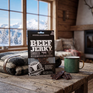 Kuivalihakundi Beef Jerky Røkt på et trebord i en hytte, med ullpledd, emaljekopp og snødekte fjell utenfor vinduet, AI-generert bilde