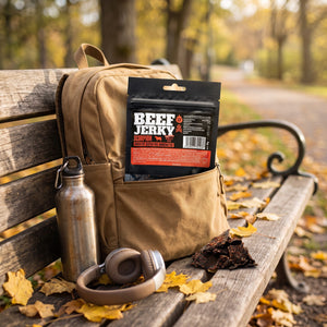 Kuivalihakundi Beef Jerky Scorpion stikker opp av en ryggsekk på en parkbenk om høsten, med drikkeflaske og hodetelefoner, AI-generert bilde