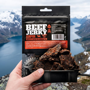 Hånd som holder Kuivalihakundi Beef Jerky Scorpion foran et fjordlandskap, AI-generert bilde