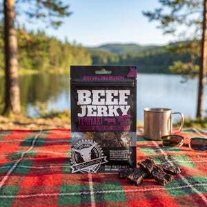 Kuivalihakundi Beef Jerky Teriyaki på et rutete piknikteppe ved et skogsvann en sommerdag, med stålkopp og solbriller, AI-generert bilde