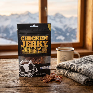 Kuivalihakundi Kylling Jerky med Sitrongress på et trebord i en hytte, med ullpledd, emaljekopp og snødekte fjell utenfor vinduet, AI-generert bilde