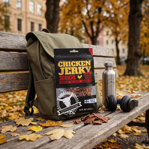 Kuivalihakundi Kylling Jerky Sriracha stikker opp av en ryggsekk på en parkbenk om høsten, med drikkeflaske og hodetelefoner, AI-generert bilde