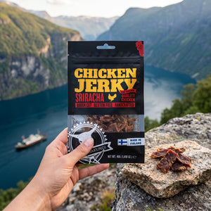 Hånd som holder Kuivalihakundi Kylling Jerky Sriracha foran et fjordlandskap, AI-generert bilde