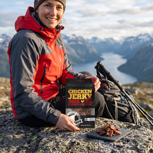 Turgåer tar en pause på fjellet og holder Kuivalihakundi Kylling Jerky Sriracha, AI-generert bilde