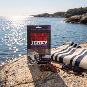 Kuivalihakundi Greasy Pork Jerky Koreansk Stil på et svaberg ved sjøen, med håndkle og solbriller, AI-generert bilde