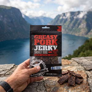 Hånd som holder Kuivalihakundi Pork Jerky Røkt BBQ foran et fjordlandskap, AI-generert bilde