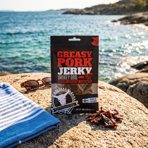 Kuivalihakundi Pork Jerky Røkt BBQ på et svaberg ved sjøen, med håndkle og solbriller, AI-generert bilde