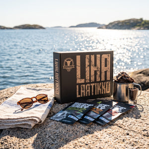 Kuivalihakundi The Meat Box 8 poser jerky på et svaberg ved sjøen, med håndkle og solbriller, AI-generert bilde