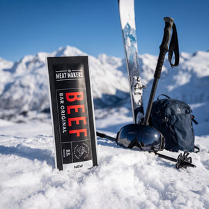 Meat Makers Beef Bar Original i snøen ved siden av turski og staver på en solrik vinterdag i fjellet, AI-generert bilde