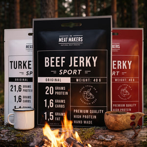 Meat Makers Sports Beef Jerky Pakkepris på en stokk ved bålet i furuskogen i skumringen, med emaljekopp og kuksa, AI-generert bilde