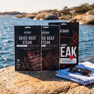 Meat Makers Tørket Oksefilet Pakkepris på et svaberg ved sjøen, med håndkle og solbriller, AI-generert bilde