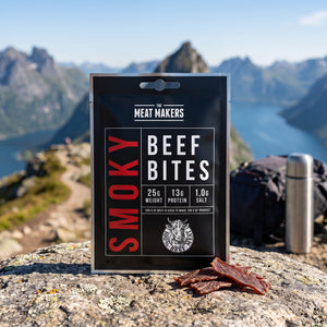 Meat Makers Røkt og tørket Oksefiletbiter på en stein ved en fjellsti høyt over fjorden, med ryggsekk og termos, AI-generert bilde