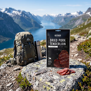Meat Makers Lufttørket Svineindrefilet på en stein ved en fjellsti høyt over fjorden, med ryggsekk og termos, AI-generert bilde