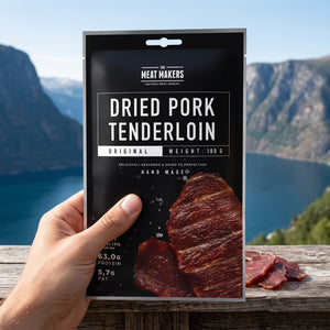 Hånd som holder Meat Makers Lufttørket Svineindrefilet foran et fjordlandskap, AI-generert bilde