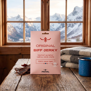 Primal Original Norsk Beef Jerky på et trebord i en hytte, med ullpledd, emaljekopp og snødekte fjell utenfor vinduet, AI-generert bilde