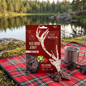 Renjer Hjort Jerky med Chili & Lime på et rutete piknikteppe ved et skogsvann en sommerdag, med stålkopp og solbriller, AI-generert bilde